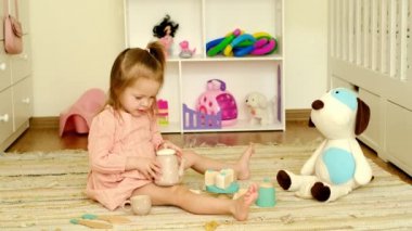 Kız çay içmece oynuyor, arkadaşına içki koyuyor oyuncak bir yavru köpek. Bebek misafirlere kibarca gülümsüyor. Tahta tabaklar ve ikramlar. Çocuklar tuvaletinde yerde oyun oynarlar.