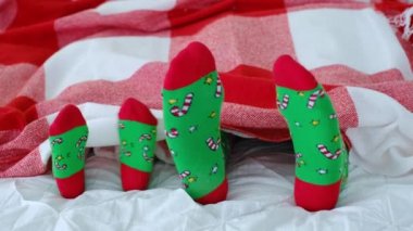 Parlak yeşil Noel çorapları içindeki çocuk ve yetişkin ayakları ekoseli kumaşın altından görülebilir. Aile tatili kış tatilinde yatakta. Büyük ve küçük ayaklar. Neşeli birlikte