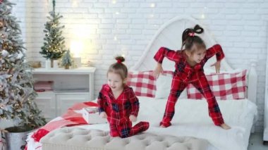 Pijamalı iki çocuk zıplar, zıplar ve komik surat yapar. Yatak odasındaki yatakta Noel ağacıyla surat asarlar. Çocuklar Noel 'in yaklaşmasına sevinirler, yeni yıla. Kış tatili eğlence içindir. xmas