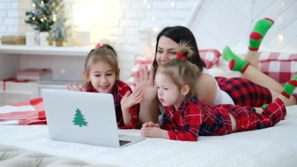 家族はこんにちは クリスマスにバーチャルズームビデオ会議コールで親戚に会う話をしていると言います 自宅でノートパソコンで一緒に距離をオンラインチャット パジャマをコンピューターでチェッカーした赤ん坊 クリスマス — ストック動画