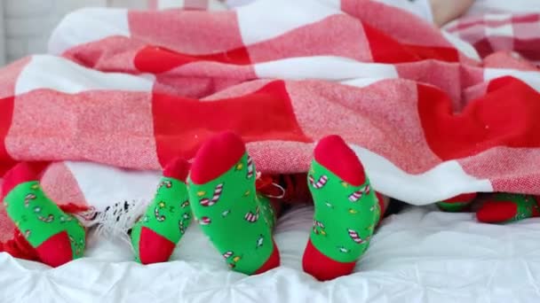爸爸和孩子们穿着一模一样的红色和绿色的圣诞袜 脚上挂着糖果手杖和星星 这家人躺在柔软的床垫上舒服的床上 从新年假期和烦恼中休息 脚特写 — 图库视频影像