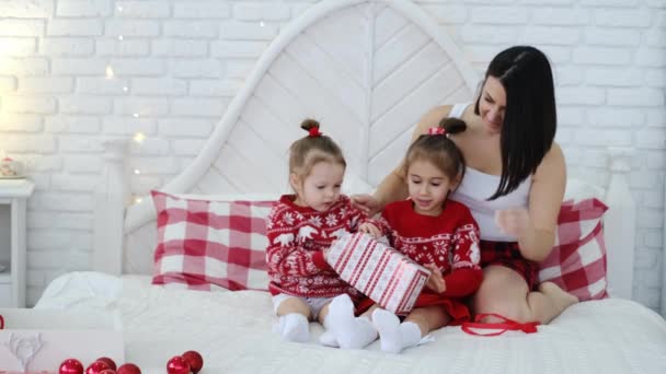 母親と女の子はベッドのベッドルームでクリスマスの赤い贈り物を包みます 驚きとプレゼントに驚かされた面白い子供たち ギフト包装箱 — ストック動画