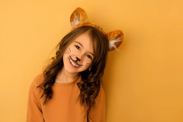 Yüzü boyalı, kulakları kulaklı, stüdyo arka planında izole bir kaplan gibi giyinmiş sevimli, komik, gülen kız. Hayvan suretinde bir çocuk. Karnaval kostümü.