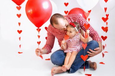Bir baba sevgililer gününde küçük kızını elinde kupa çelengiyle kırmızı bir top tutarak öper. Kız kalp şeklinde lolipop emiyor. Şefkat ve babalar ve çocukların ilişkileri