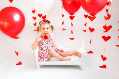 At kuyruklu kız büyük kırmızı kalp şeklinde lolipopu olan küçük bir beşikte oturuyor. Sevgililer Günü için kalpli balon ve çelenk süslemeleri.