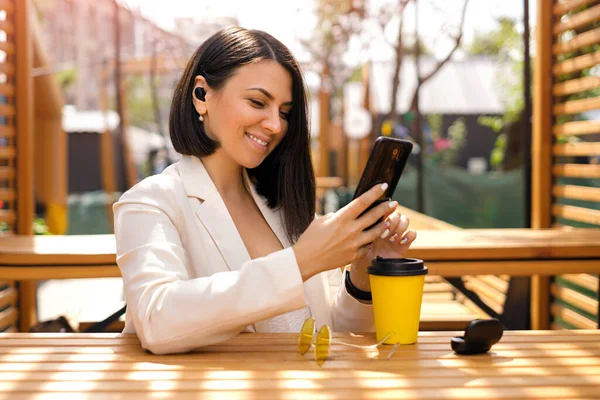 헤드폰을 브루넷 코카서스 사업가는 웃으면서 전화를 메시지를 읽는다 테라스에 카페에서 스톡 사진