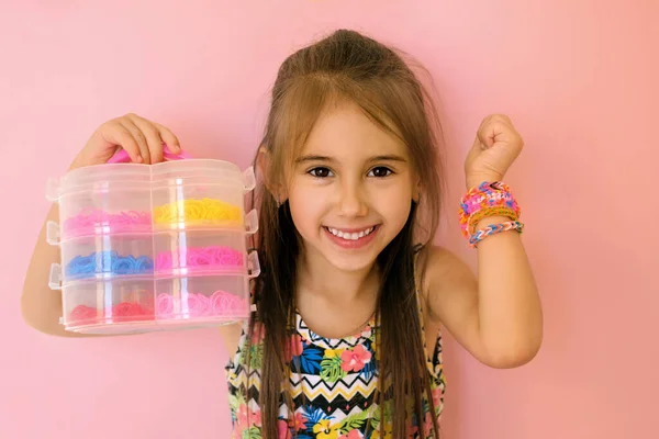 A pretty girl with braided bracelets on her wrist holds in her hand a container with a set of everything necessary for weaving accessories