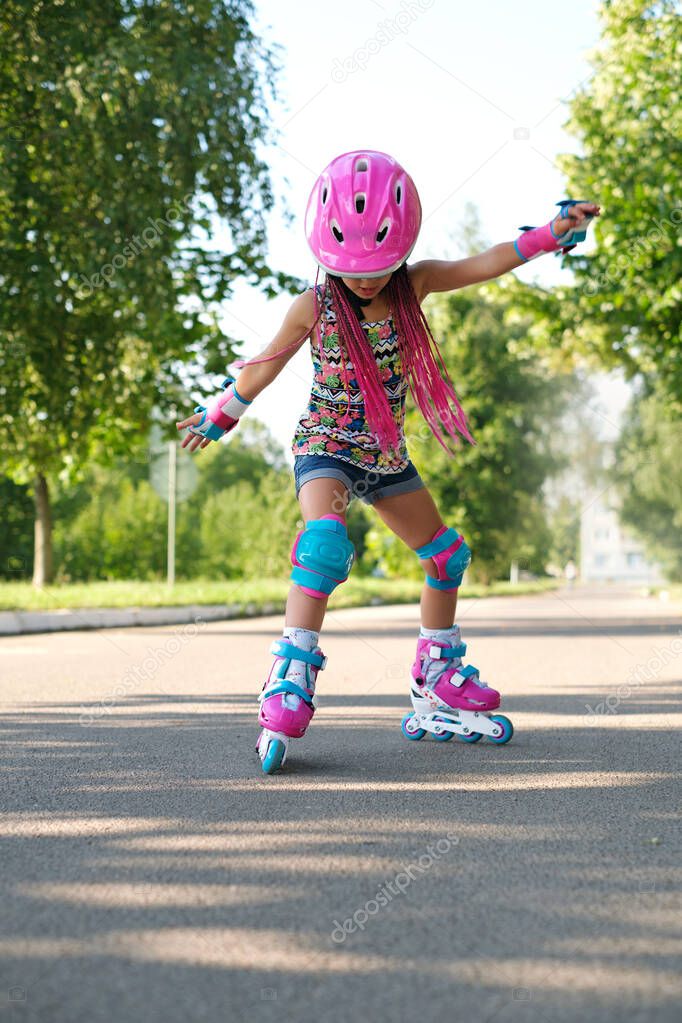 The child tries to keep his balance and not fall, for the first time standing on roller skates. A girl is learning to rollerblade. Active sports for summer recreation and outdoor entertainment