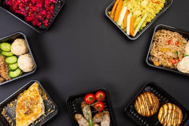 Sağlıklı yemek servisi menüsünü beslenme çantalarında hazırla et ve sebze paketleri siyah masa arkasında.