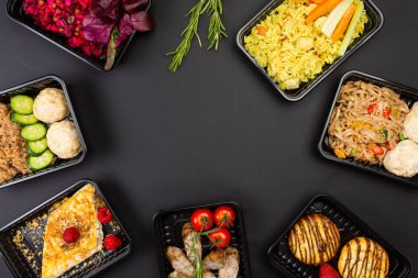 Sağlıklı yemek servisi menüsünü beslenme çantalarında hazırla et ve sebze paketleri siyah masa arkasında.