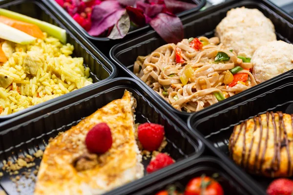 Sağlıklı yemek servisi menüsünü beslenme çantalarında hazırla et ve sebze paketleri siyah masa arkasında.