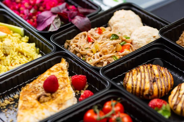 Sağlıklı yemek servisi menüsünü beslenme çantalarında hazırla et ve sebze paketleri siyah masa arkasında.