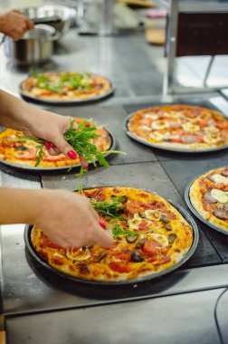 Pizza yapma süreci. Kadın taze roka ile pizzayı süslüyor.