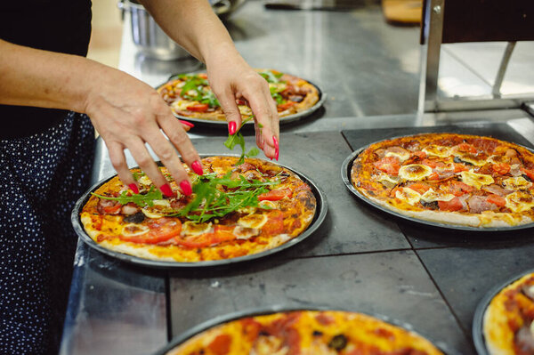 The process of making pizza. Woman decorates pizza with fresh arugula