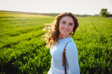 Kıvırcık esmer, yaz günlerinde gün ışığından hoşlanır. Açık havada gülümseyen güzel bir kızın portresi. Rüzgarla savrulan kıvırcık saçlarıyla sokakta dikilen genç bir kadın yüzünü kapatıyor..