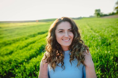 Kıvırcık esmer, yaz günlerinde gün ışığından hoşlanır. Açık havada gülümseyen güzel bir kızın portresi. Yeşil arka planda gülümseyen çilli genç kadın..