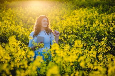 Mutlu kız sarı çiçeklerin arka planında İncil 'e sarılıyor. Açık havada kitap okuyan bir kız. İnanç, maneviyat ve din kavramı. Barış, umut