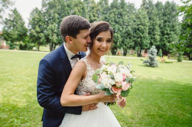 Parkta yürüyüş yapan güzel bir çift. Açık havada gelinlerin nazikçe kucaklaşması. Gelin ve damat yeşil bahçede öpüşüyor. Düğün günü. Mutlu ve neşeli bir an.