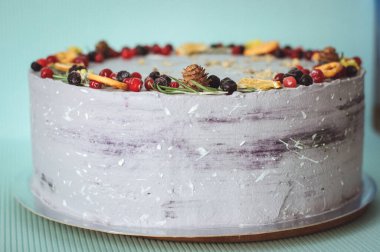 Yaban mersini, kızılcık, portakal ve koni ile süslenmiş menekşe kremalı pasta. Mavi arka planda gri yuvarlak pasta, yeni yıl tarzında dekore edilmiş.