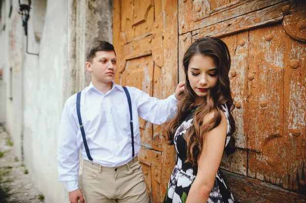 若い男は 古い茶色のドアの背景を背景に 彼の最愛の女の子の髪をまっすぐにします 街を歩くカップルを愛する — ストック写真