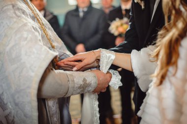 Gelin ve damadın elleri düğün havlusuyla bağlandı, yaklaşın. Rahip gelinin el havlusunu bağlar. Kilisedeki düğün töreninde gelinler