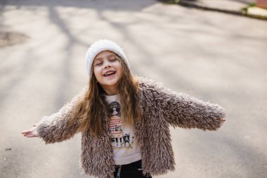 Bahar güneşinin tadını çıkarırken gözlerini kapatan uzun sarı saçlı güzel bir kızın portresi. Hafif arka planda modaya uygun bir bebek. Dört yaşındaki güzel çocuk dışarıda eğleniyor. D vitamini