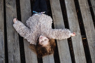 Tahta bir arka planda yatan mutlu küçük bir kızın portresi. Güzel bebek parkta yürümekten hoşlanıyor. Modaya uygun çocuklar..