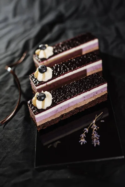 Three chocolate cakes on a black background. Mousse cake with blueberries. Opera cake at the a La carte desserts , cakes on a black background. Selective focus