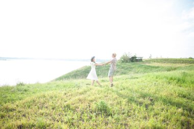 Sevgi dolu bir çift zıplıyor ve birbirlerinin elini tutuyor. Nehir ve gökyüzünün zeminine karşı. Çelenkli güzel bir kız ve şapkalı şık bir adam güneşli bir günde dışarıda vakit geçirir. Aşk hikayesi..