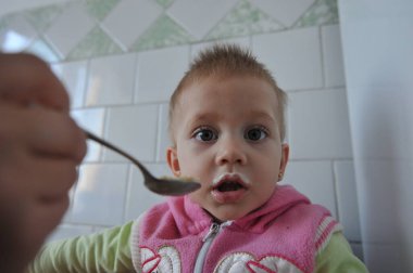 Anne bebeği kaşıkla besliyor, yakın plan. Bir yaşında bir çocuk yulaf lapası yer. İlk diş