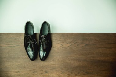 Kahverengi ahşap tahtada siyah erkek ayakkabısı ve katı beyaz zeminin üst görüntüsü. Erkek aksesuarları. Siyah cilalı deri ayakkabılar, klasik ayakkabılar. Boşluğu kopyala.