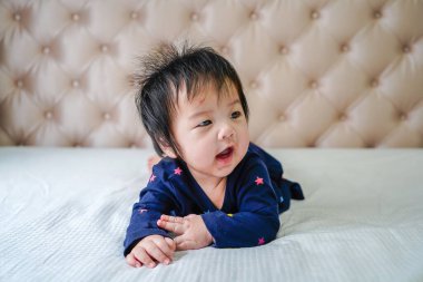 Evde, yatakta oynayan tatlı küçük bir kız bebek. Evdeki yatakta uzanmış şirin beyaz bir bebek. Küçük tatlı kız, mavi elbiseli çocuk, beyaz güneşli, parlak yatak odasında kameraya mutlu bir şekilde gülümsüyor..