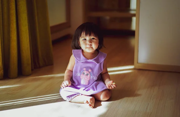 ベビーガールの肖像画は 床に座っている紫色のドレスを着用し 光と影の反射と空の部屋でカメラに笑顔 光と影の概念 カメラを見ると — ストック写真