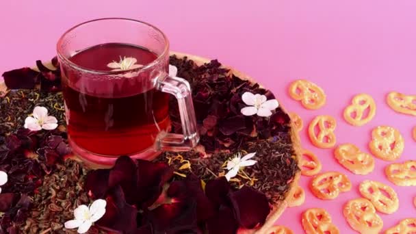 Flower tea in glass mug slowly rotates in pink lighting on pink background. — Stock video