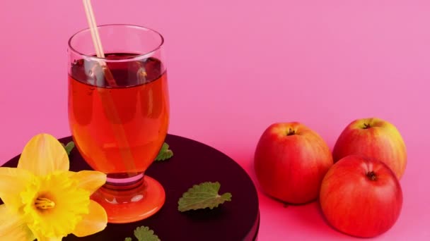 Яблучний сік або сидр у прозорому склі повільно обертаються на поворотному столі і три свіжих яблука біля рожевого світла . — стокове відео