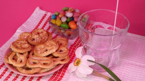 Pouring fresh farm milk into glass next to pretzels and candies. With pink light. — Vídeo de stock
