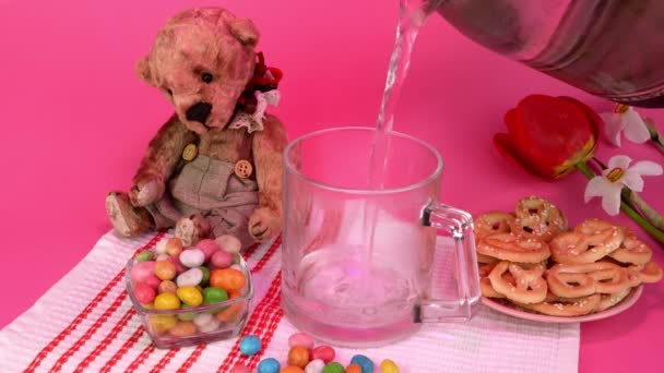 在椒盐饼干、糖果和泰迪熊旁边，把热茶倒入杯子里。粉红的灯光. — 图库视频影像