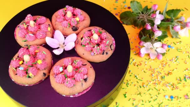 Cookie decorated with vanilla cream rotate slowly on black turntable in pink light. Sweets and desserts made on domestic kitchen. — ストック動画