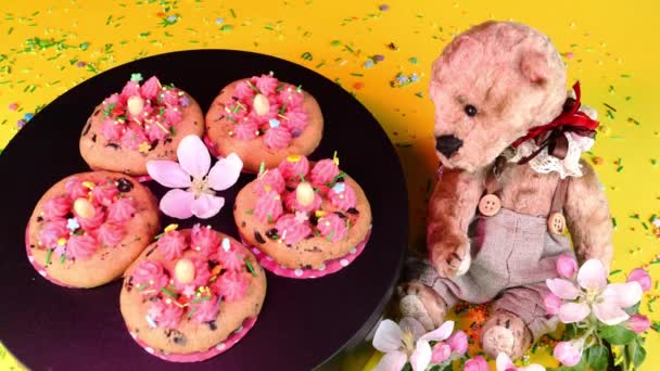 Cookie decorated with vanilla cream rotate slowly on black turntable in pink light. Teddy bear. Sweets and desserts made on domestic kitchen. — ストック動画
