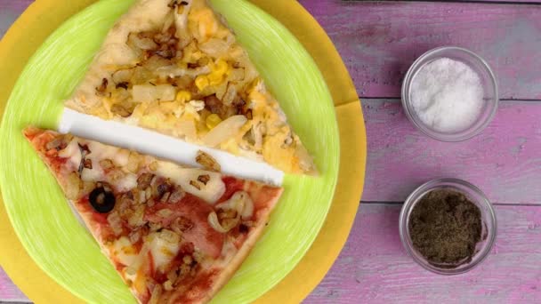 Deux morceaux de pizza aux tomates, saucisse, mozzarella et olives sur assiette tournent lentement sur fond rose. — Video