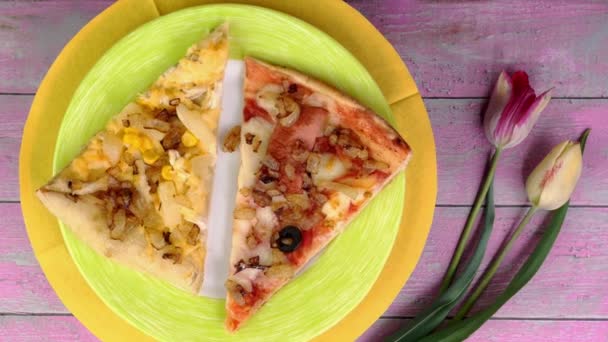 Два куска пиццы с помидорами, колбасой, моцареллой и оливками на тарелке медленно вращаются на розовом фоне. — стоковое видео