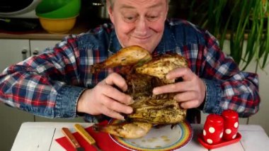 Senior adult man with appetite eating toasted fried chicken at table in home kitchen.