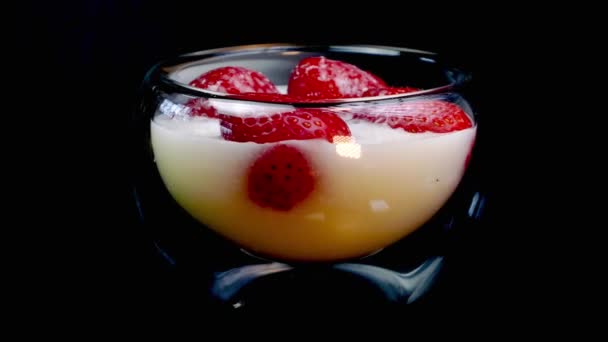 草莓中倒入奶油或酸奶，在玻璃碗的黑色背景上慢慢旋转. — 图库视频影像
