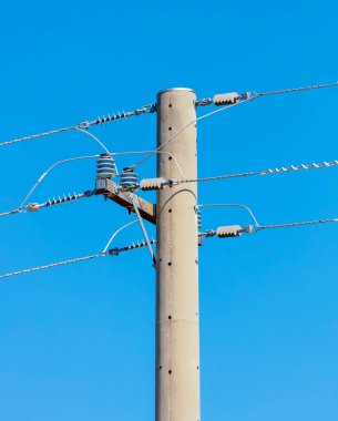Beton bir telefon direğinin ve mavi gökyüzüne bağlı kabloların fotoğrafı.