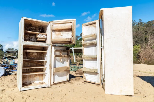 Photograph of severely flood damaged refrigerators on a white sandy area of land near the Hawkesbury river in New South Wales in Australia