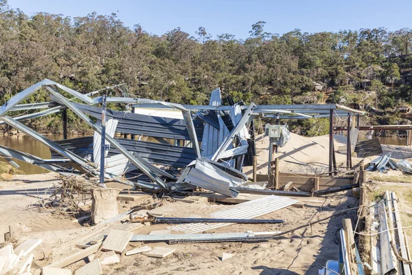 Photograph of a severely flood damaged outdoor building on a white sandy area of land near the Hawkesbury river in New South Wales in Australia