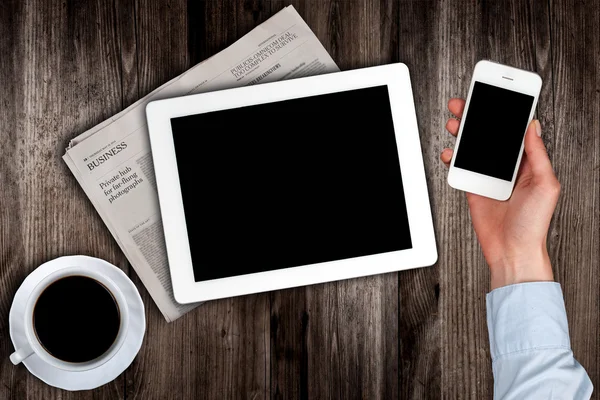 Smartphone in der Hand und eine Zeitung mit dem Tablet auf dem Tisch — Stockfoto