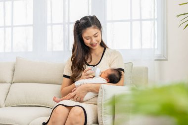 Yeni doğan bebek annesinin kollarında süt içiyor. Güzel Asyalı anne kucağında bebeği sevgiyle besliyor. Anne ve yeni doğan kavramı.