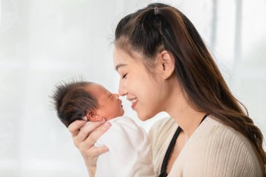 Güzel, Çekici Asyalı anne yeni doğmuş bebeğini elinde tutuyor ve bebek burnunu tatlı ve sevimli bir şekilde öpüyor. Mutlu anne ve bebek birlikte gülümsüyor. Anne ve yeni doğan bebek kavramı.