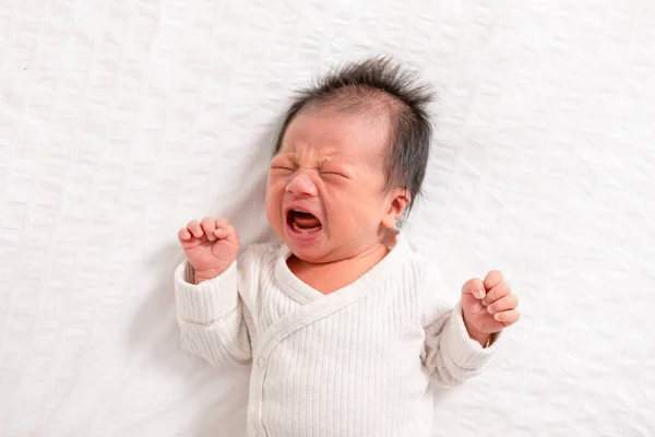 Crying Newborn baby boy lying on white bed at home.Infant baby screaming very hungry or stomach pain.Tired baby crying concept